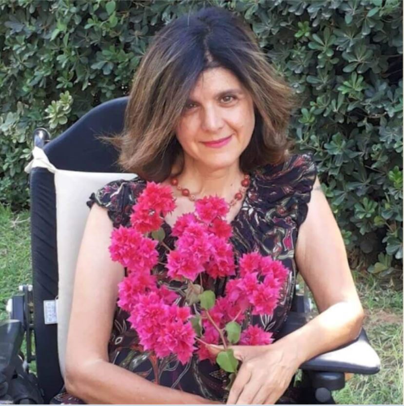 צילום של עינת קדם, עורכת לשונית, עורכת ספרותית, עורכת אקדמית, מחזיקה ענף משיח עם פרחים ורודים.