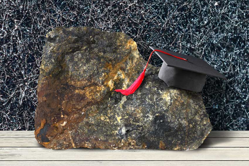 כובע מסיימי תואר אקדמי מונח על אבן סלע גדולה, על רקע צילום תקריב של סיבי מטלית ניקוי, מדגימים עריכה מדעית איכותית כבסיס יציב לעבודה אקדמית טובה.