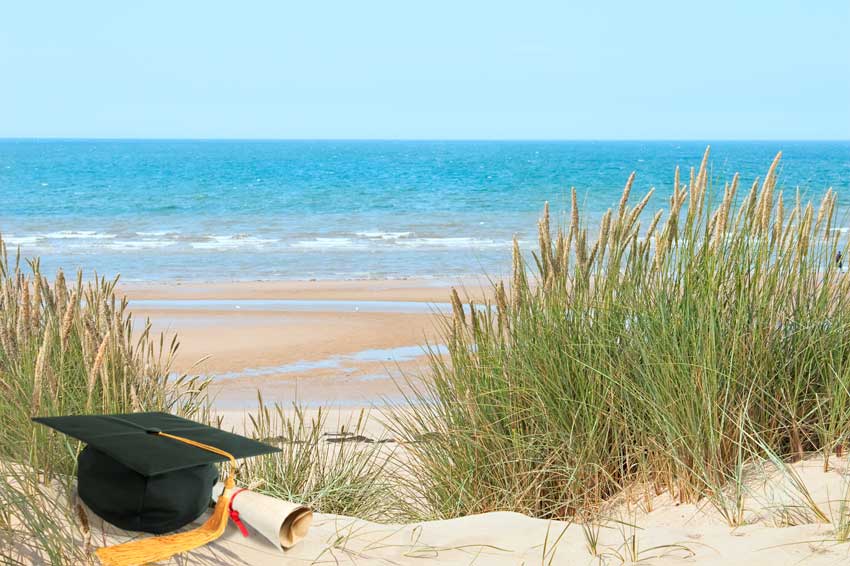 כובע בוגרים למסיימי תואר אקדמי ודיפלומה בחוף פומבי באנגליה מול הים, מדגימים עריכה לשונית של עבודה מדעית המתאימה את הסגנון לעולם הכתיבה המדעי המחקרי.