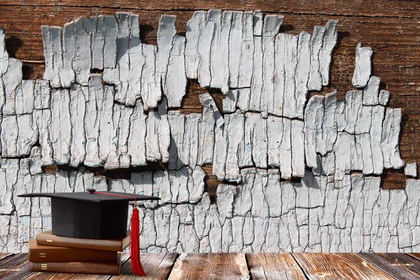 כובע בוגרים למסיימי תואר אקדמי וספרים, על רקע צילום תקריב של מרקם עץ ישן עם צבע מתקלף מדגימים עריכה לשונית מקצועית המסייעת לחוקרים במלאכת צילום התקריב של מושא מחקרם.