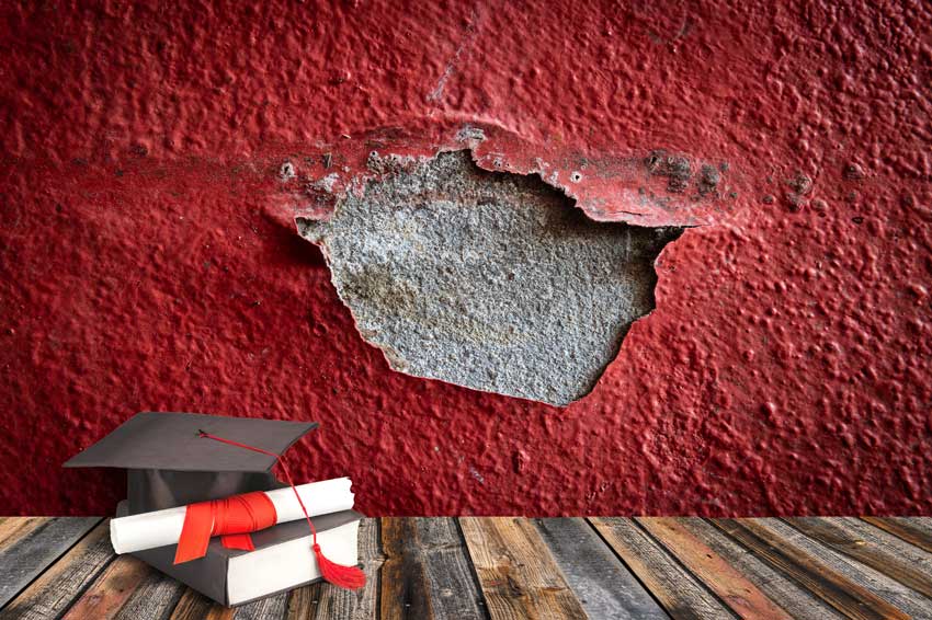 כובע מסיימי תואר אקדמי ודיפלומה על רקע קיר אדום עם צבע מתקלף, החושף חלק אפור ללא צבע, מדגימים עריכה מדעית מקצועית המתארת את המחקר ואת יסודותיו, שלב אחר שלב.