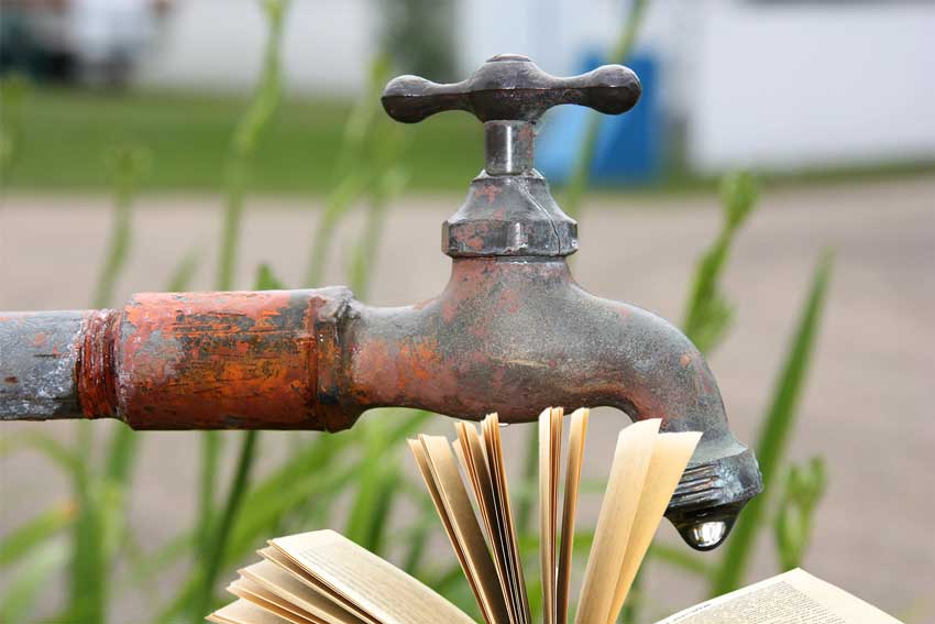 ברז מים ישן בחצר עם טיפת מים, מעל ספר פתוח מדגים טפטוף מבוקר בעריכה ספרותית.