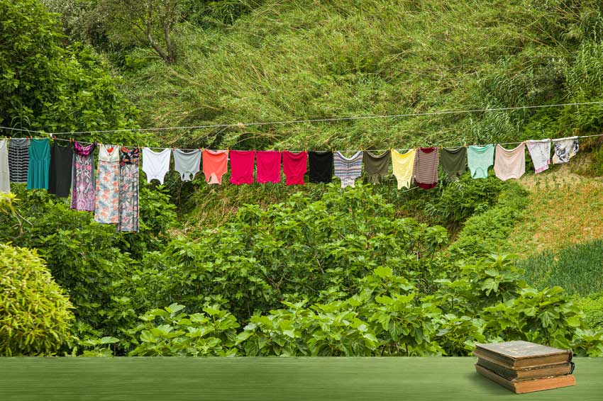 חבל עם כביסה צבעונית מעל נוף הררי ירוק וספרים, מדגימים עריכה ספרותית המתכננת כל מהלך.