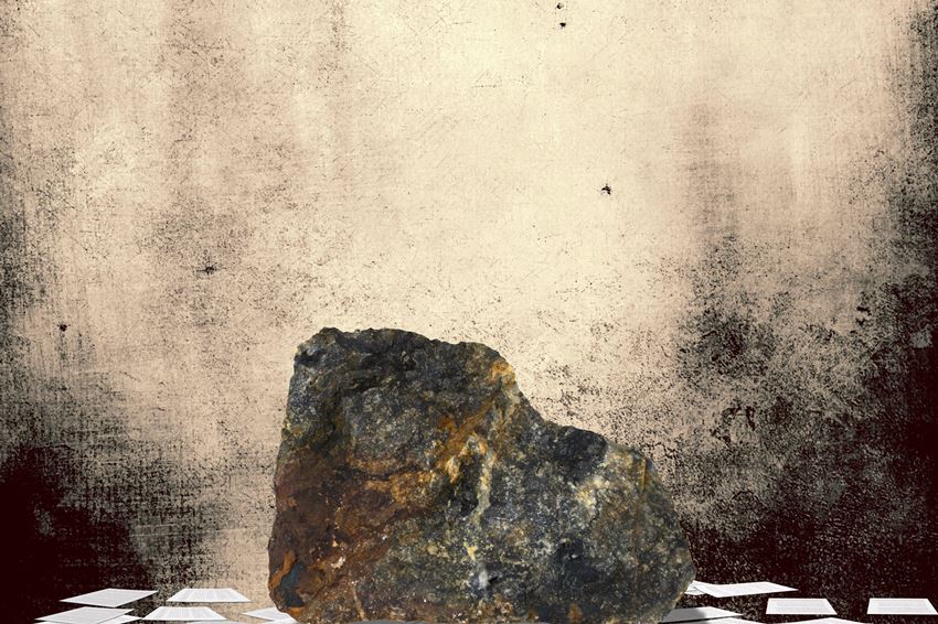 אבן כבדה ומחוספסת מונחת על ערמת דפי עריכה מייצגת עריכה לשונית על טקסט גולמי לפני עריכת ליטוש.